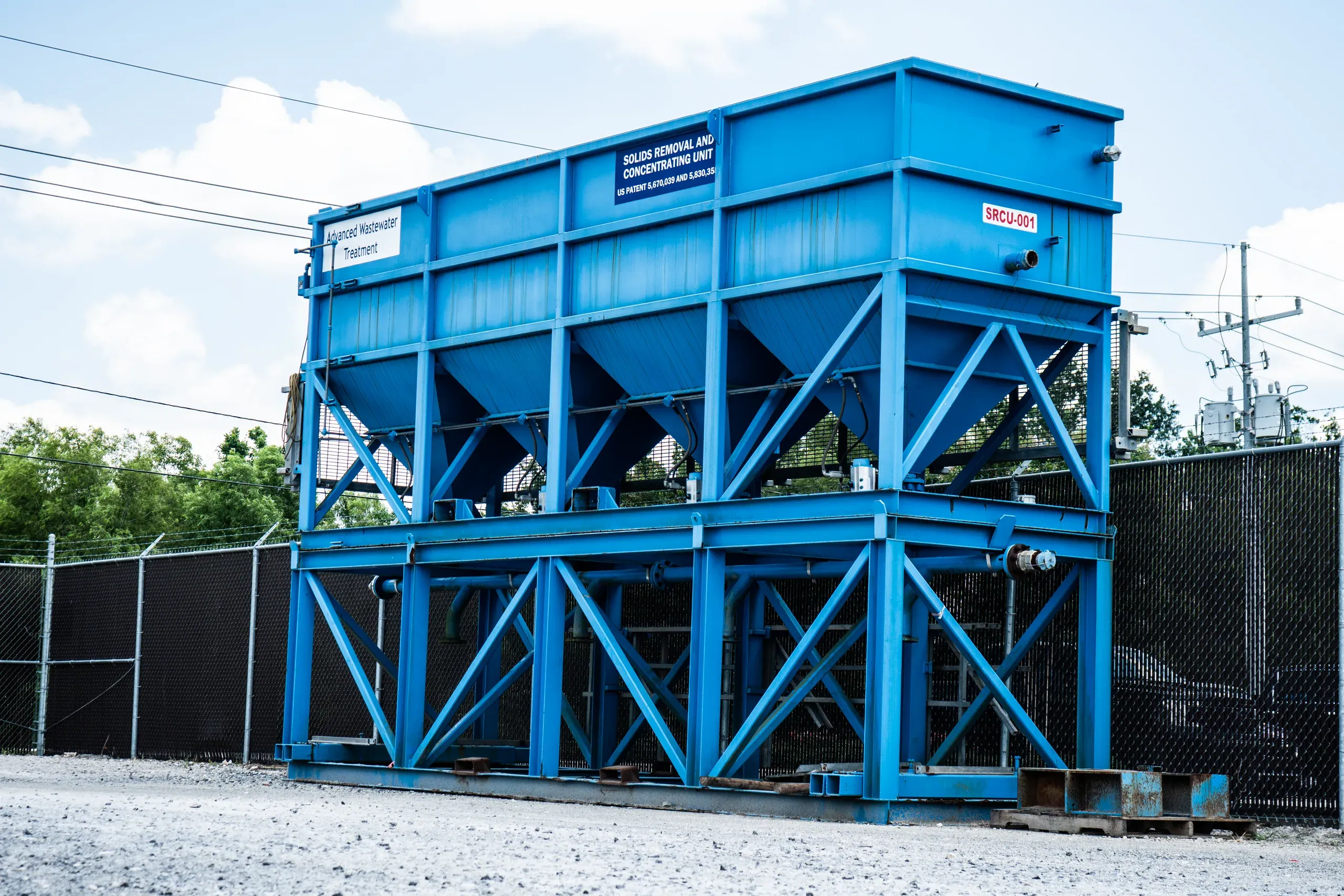 Blue elevated solids removal and concentrating unit on a cross-braced steel frame standing in the Spectrum yard against a bright sky